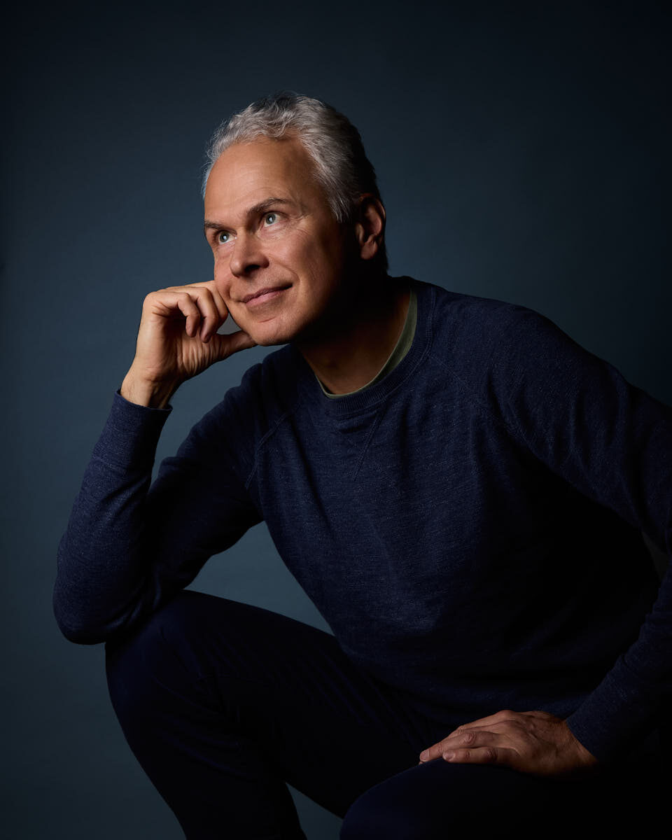 Självporträtt av Martin Ekwall, sittande med handen mot kinden mot mörkblå bakgrund, tittar åt sidan snett uppåt. För Photo for Brands