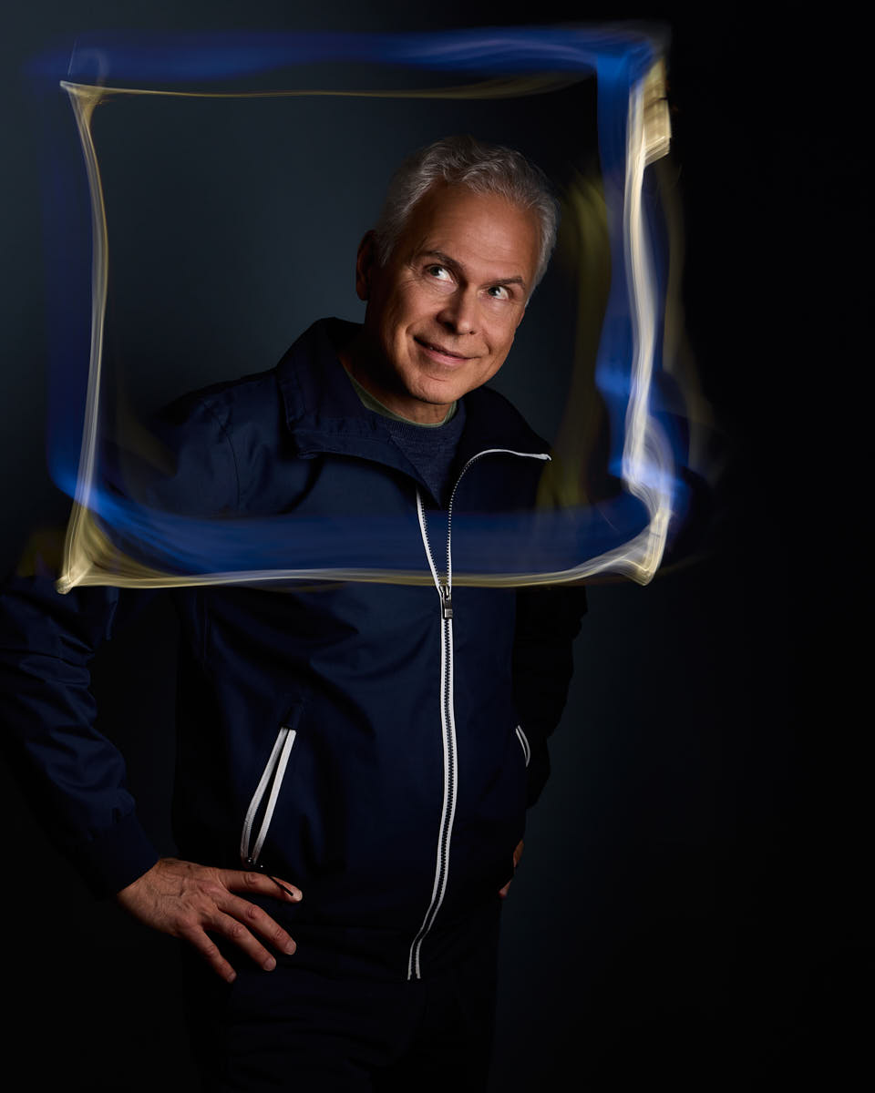 Självporträtt av Martin Ekwall, stående mot mörkblå bakgrund tittandes åt sidan genom lysande gul och blå ram. För Photo for Brands